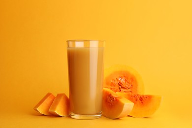 Photo of Tasty pumpkin juice in glass and cut pumpkin on orange background