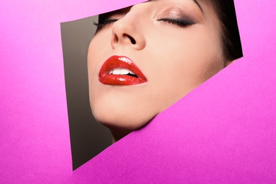 Photo of View of beautiful young woman with red lips through cutout in color paper