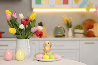 Bouquet of tulips, painted eggs and Easter decorations on white table in kitchen. Space for text