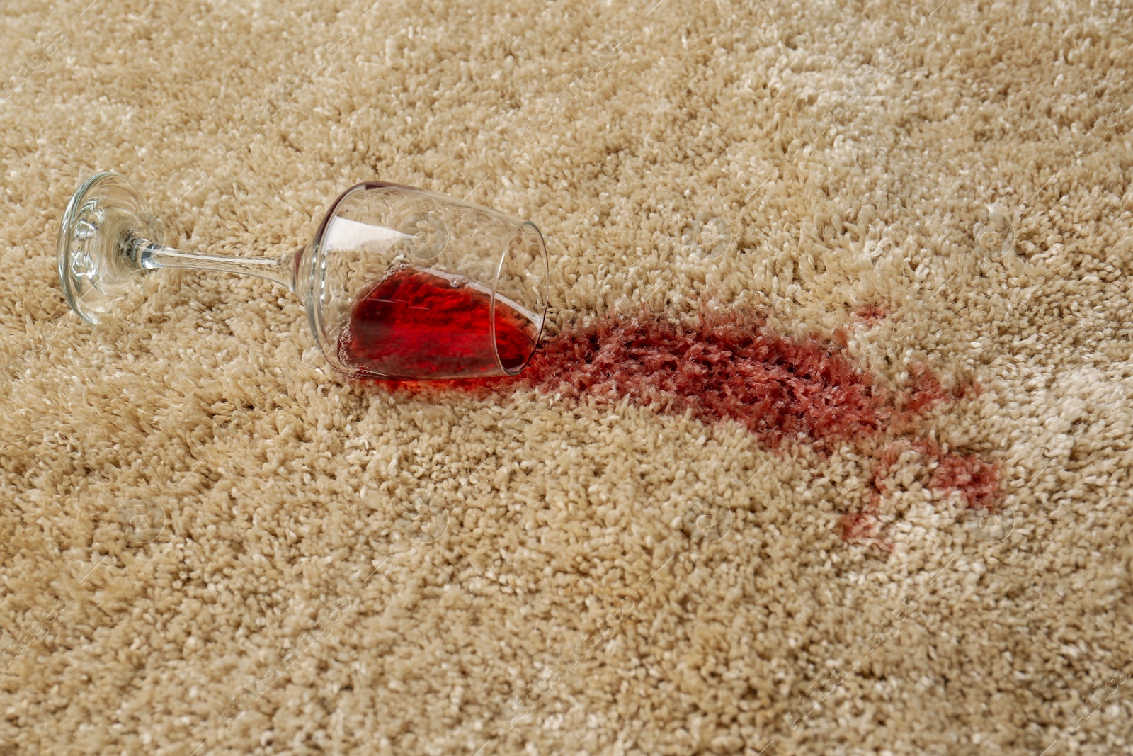 Photo of Overturned glass and spilled red wine on soft carpet