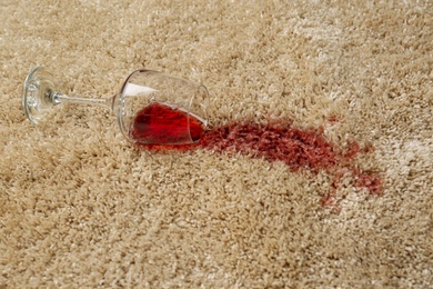 Overturned glass and spilled red wine on soft carpet