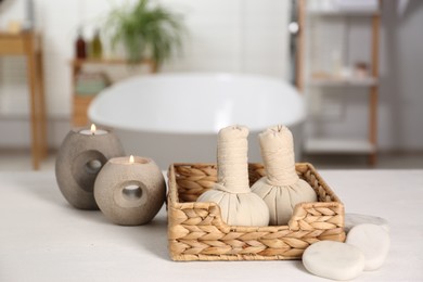 Photo of Burning candles, spa herbal bags and stones on white table in bathroom