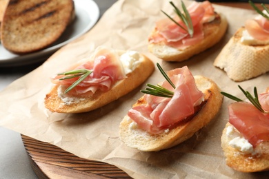 Photo of Tasty bruschettas with prosciutto and cream cheese on board, closeup