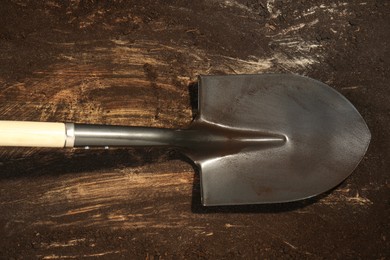 Photo of Metal shovel with fertile soil on dirty wooden surface, top view