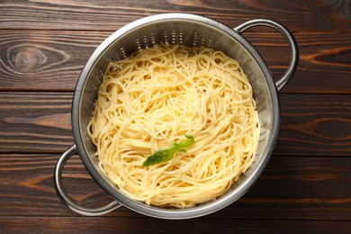 Cooked pasta in metal colander on wooden table, top view