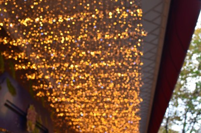 Photo of Blurred view of beautiful lights hanging from ceiling outdoors. Bokeh effect