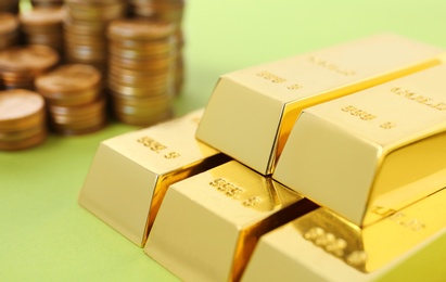 Photo of Stacked gold bars and coins on color background, closeup
