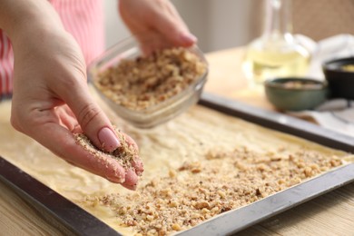 Photo of Making delicious baklava. Woman adding chopped nuts to dough at wooden table, closeup