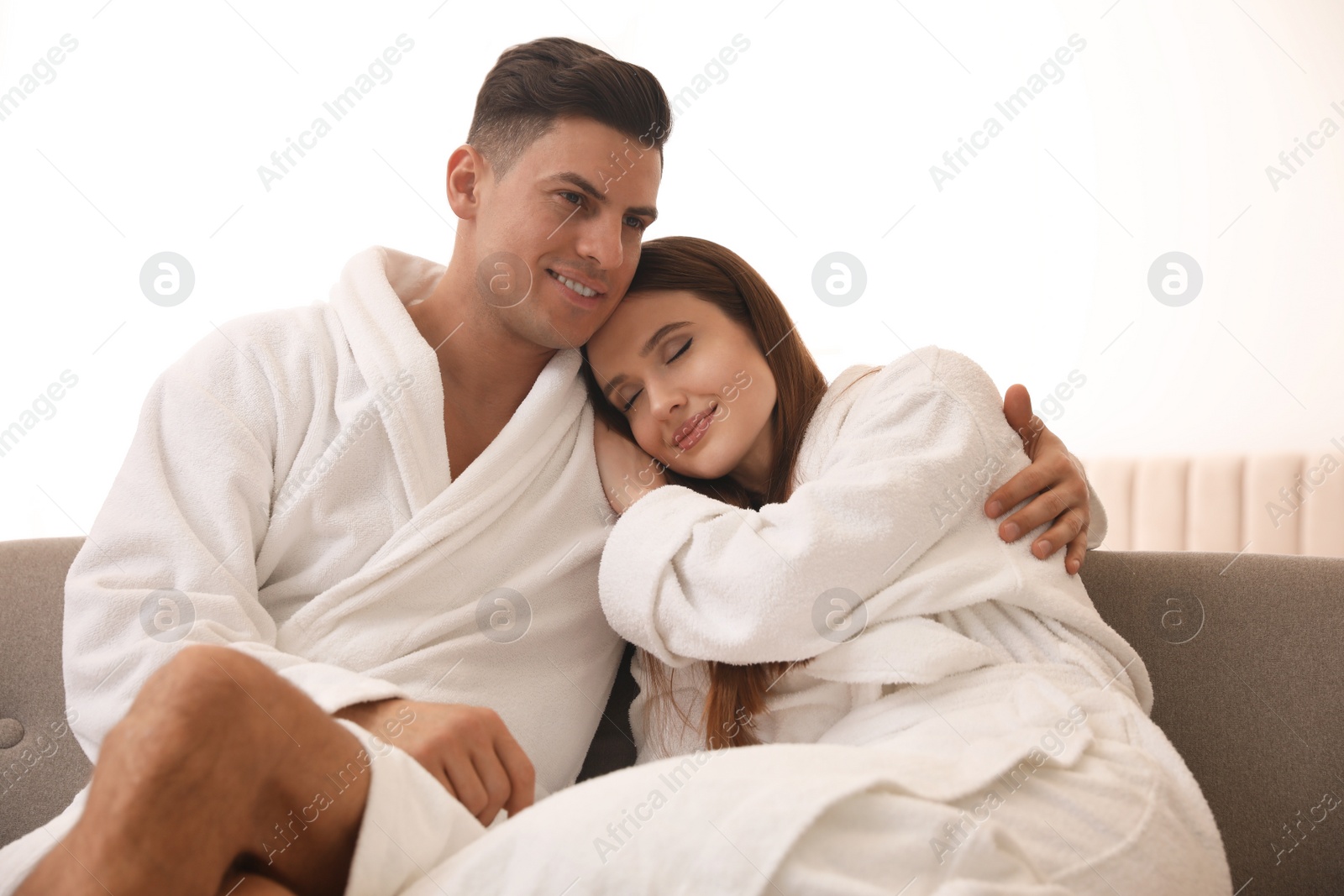 Photo of Happy couple in bathrobes on sofa at home