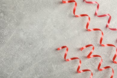 Photo of Shiny red serpentine streamers on grey background, flat lay. Space for text