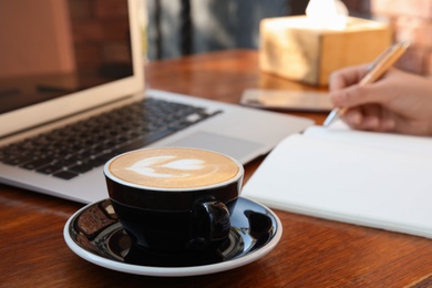 Photo of Blogger working at table in cafe, focus on cup of coffee