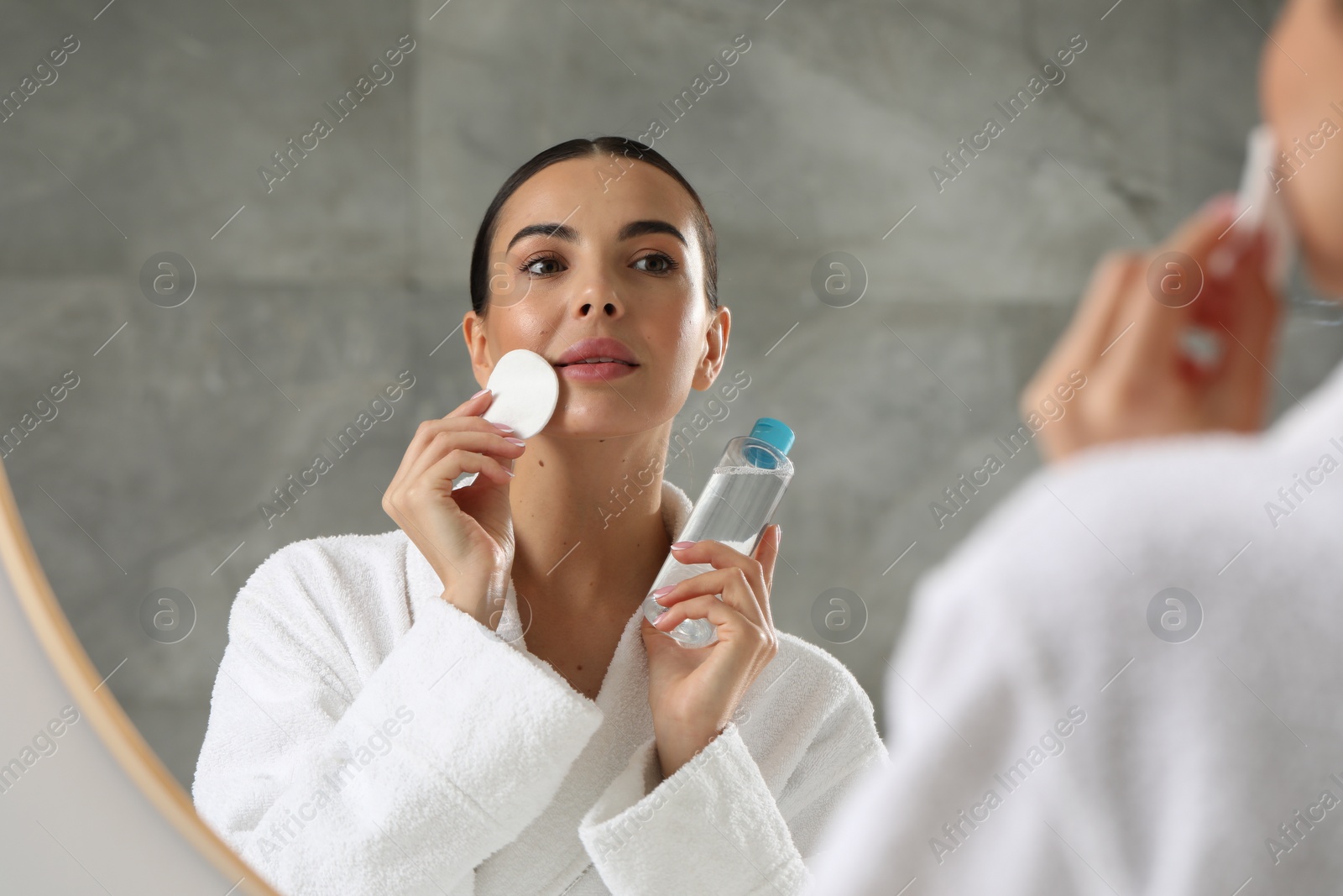 Photo of Beautiful woman removing makeup with cotton pad near mirror indoors