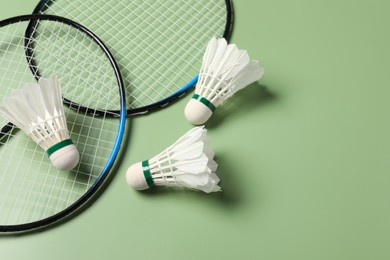 Photo of Feather badminton shuttlecocks and rackets on green background, above view. Space for text