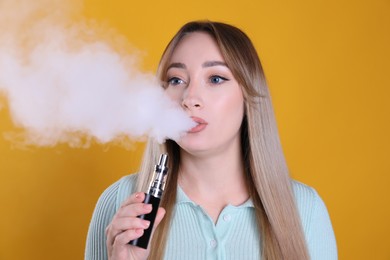 Young woman using electronic cigarette on orange background