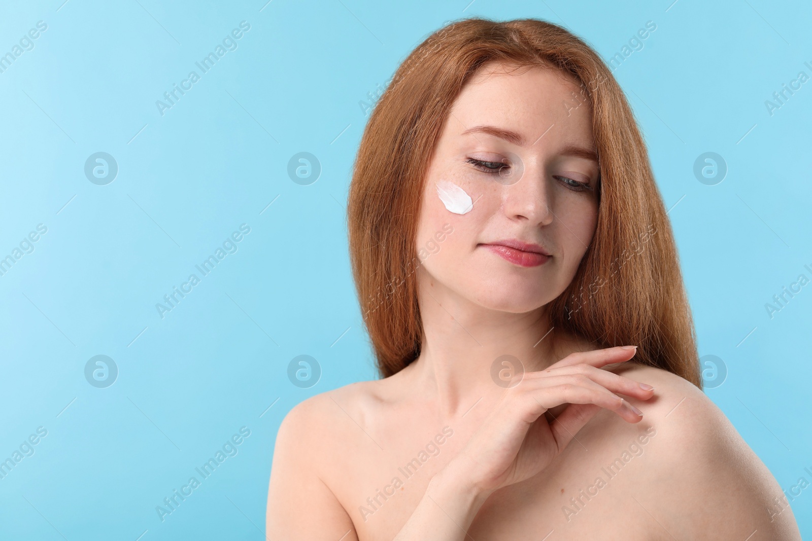 Photo of Beautiful woman with freckles and cream on her face against light blue background. Space for text