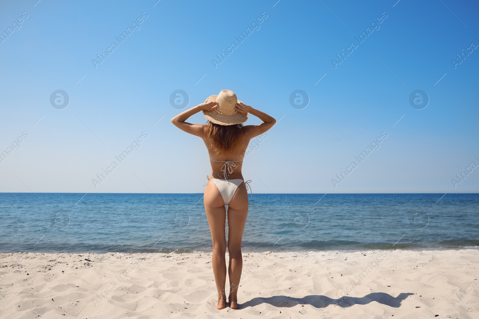 Photo of Woman with perfect body in bikini on sandy beach near sea, back view