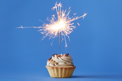 Photo of Cupcake with burning sparkler on light blue background