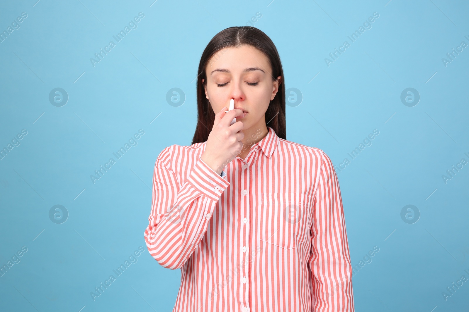 Photo of Woman using nasal spray on light blue background