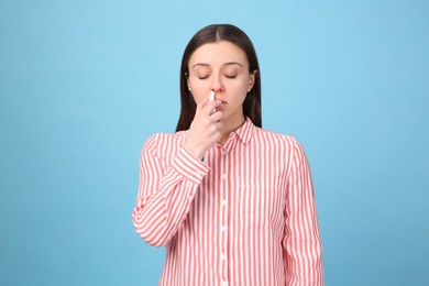 Woman using nasal spray on light blue background