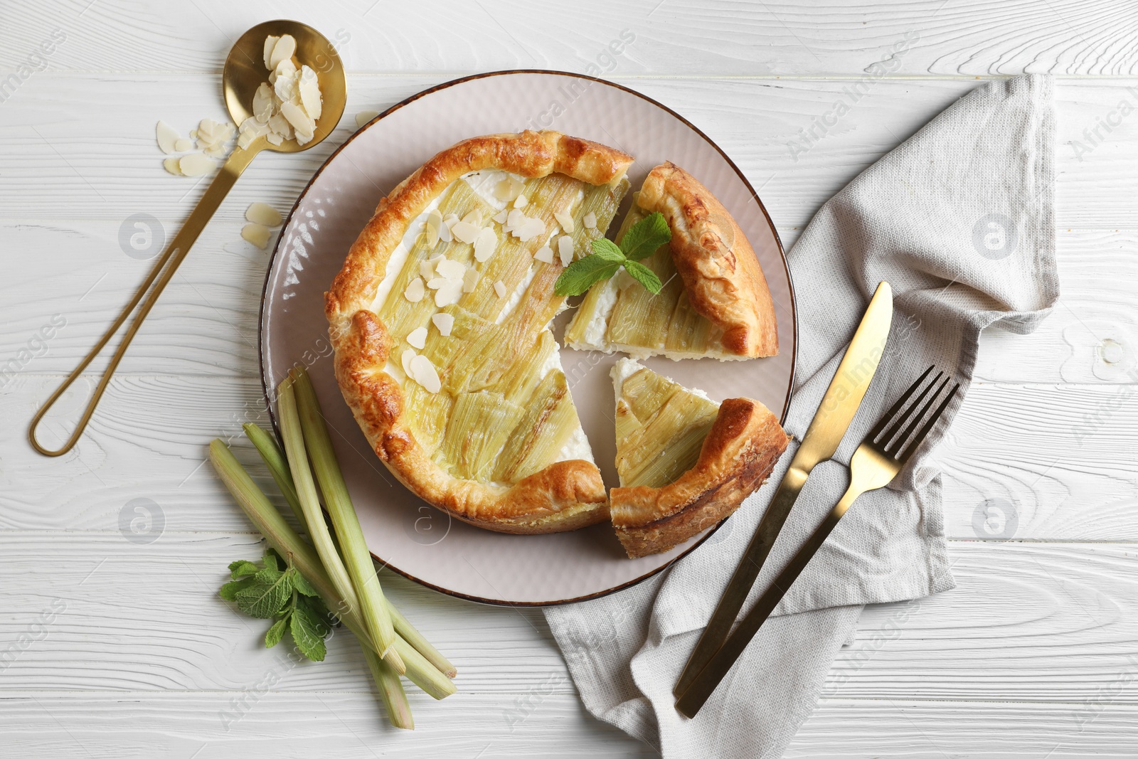 Photo of Freshly baked rhubarb pie, stalks, almond flakes and cutlery on white wooden table, flat lay