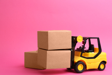 Forklift model and carton boxes on pink background. Courier service