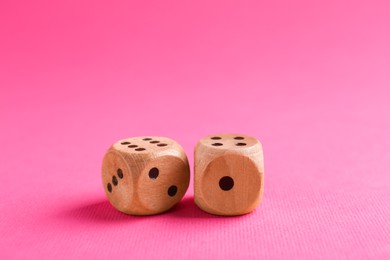 Photo of Two wooden game dices on pink background, closeup
