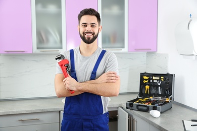 Photo of Male plumber with pipe wrench in kitchen. Repair service