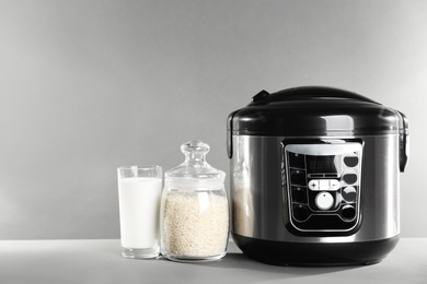 Photo of Modern powerful multi cooker and products on table against grey background. Space for text