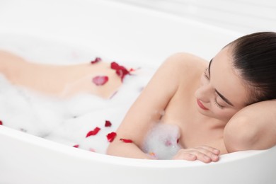 Photo of Woman taking bath in tub with foam and rose petals