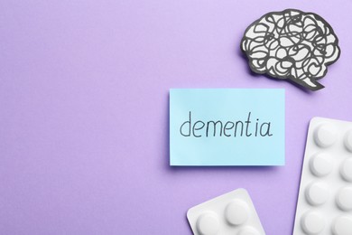 Photo of Note with word Dementia, brain cutout and pills on violet background, flat lay. Space for text