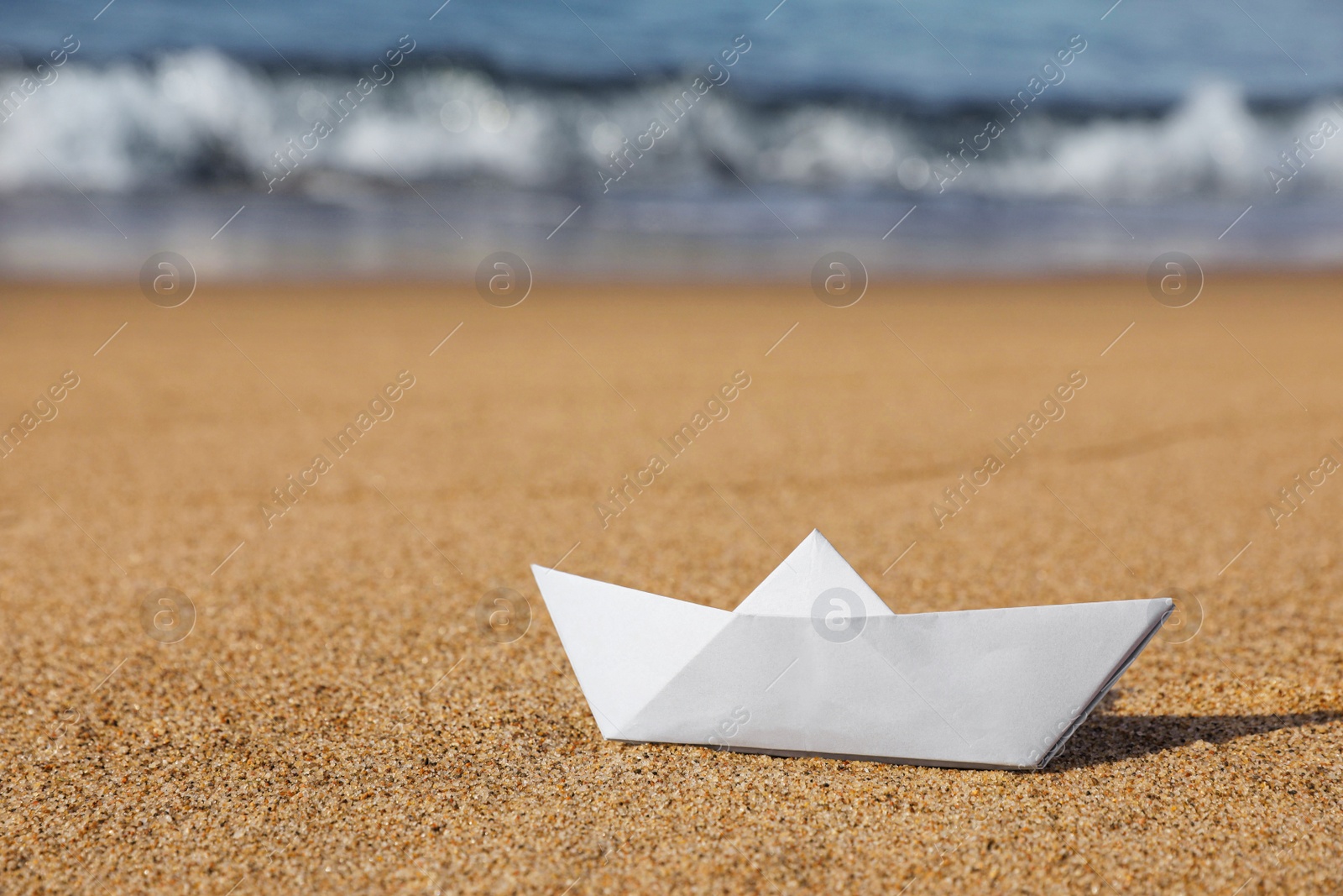 Photo of White paper boat near sea on sandy beach, space for text