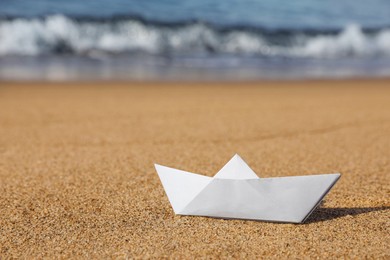 Photo of White paper boat near sea on sandy beach, space for text