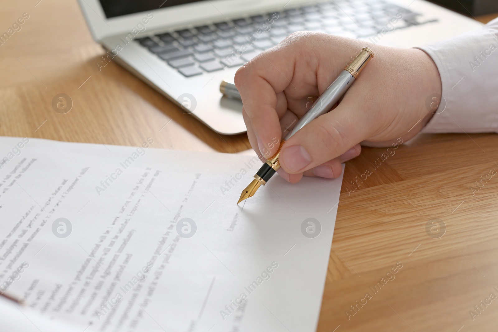 Photo of Notary signing document at wooden table, closeup