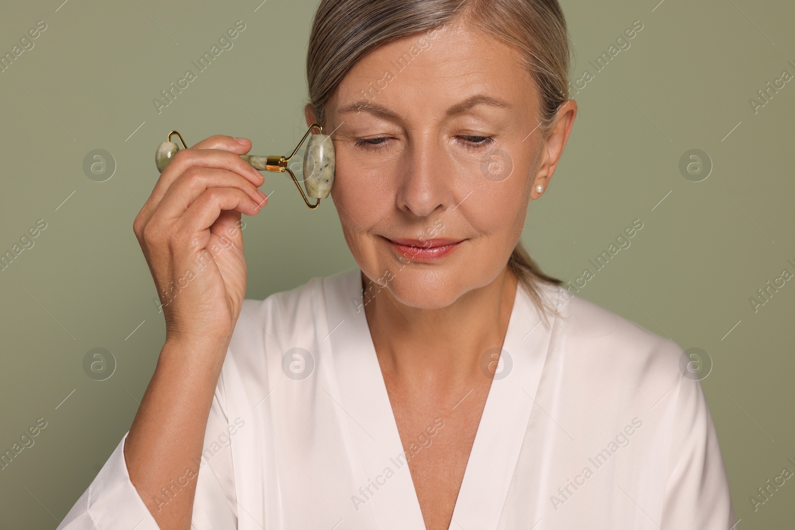 Photo of Woman massaging her face with jade roller on green background