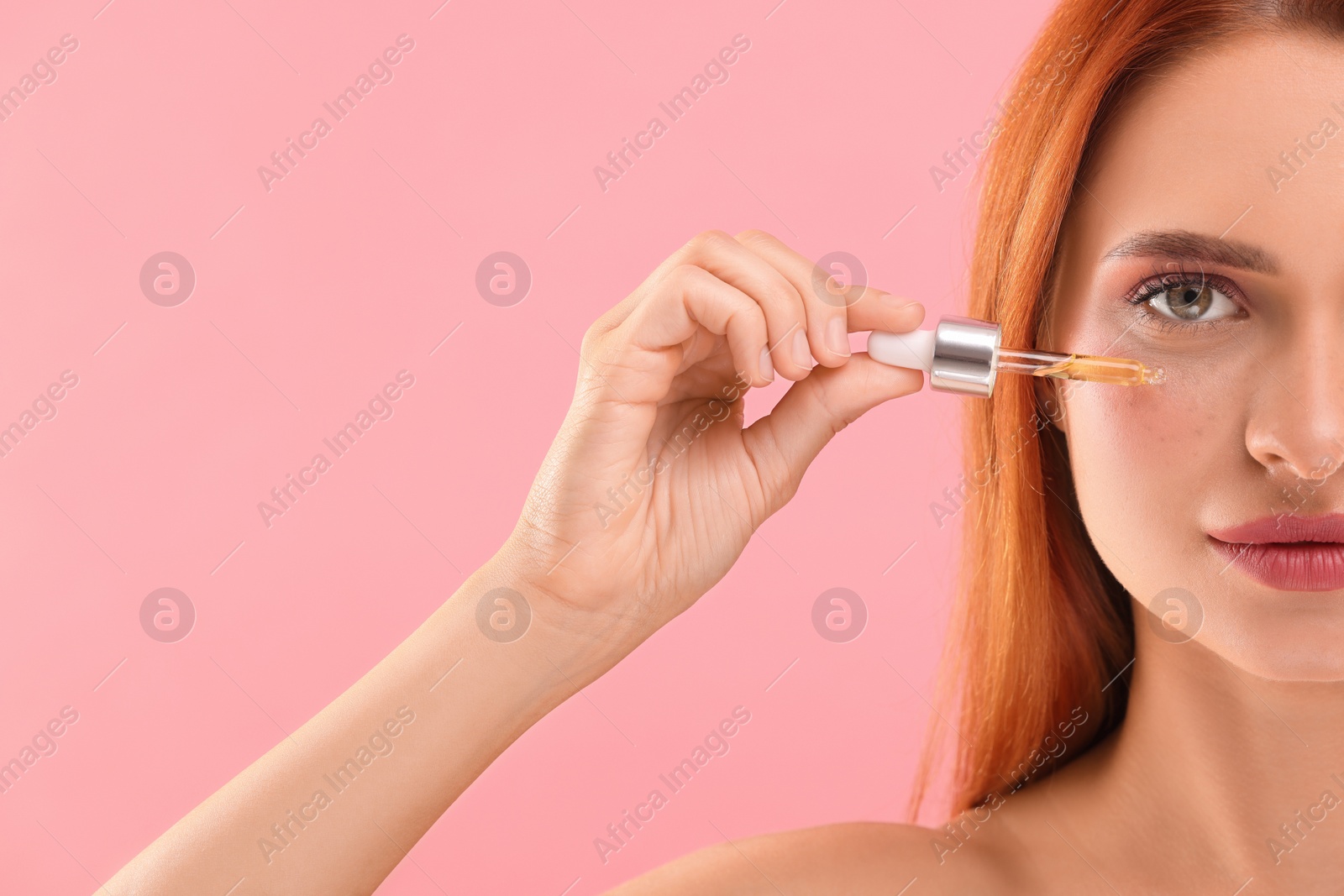 Photo of Beautiful young woman applying cosmetic serum onto her face on pink background, closeup. Space for text