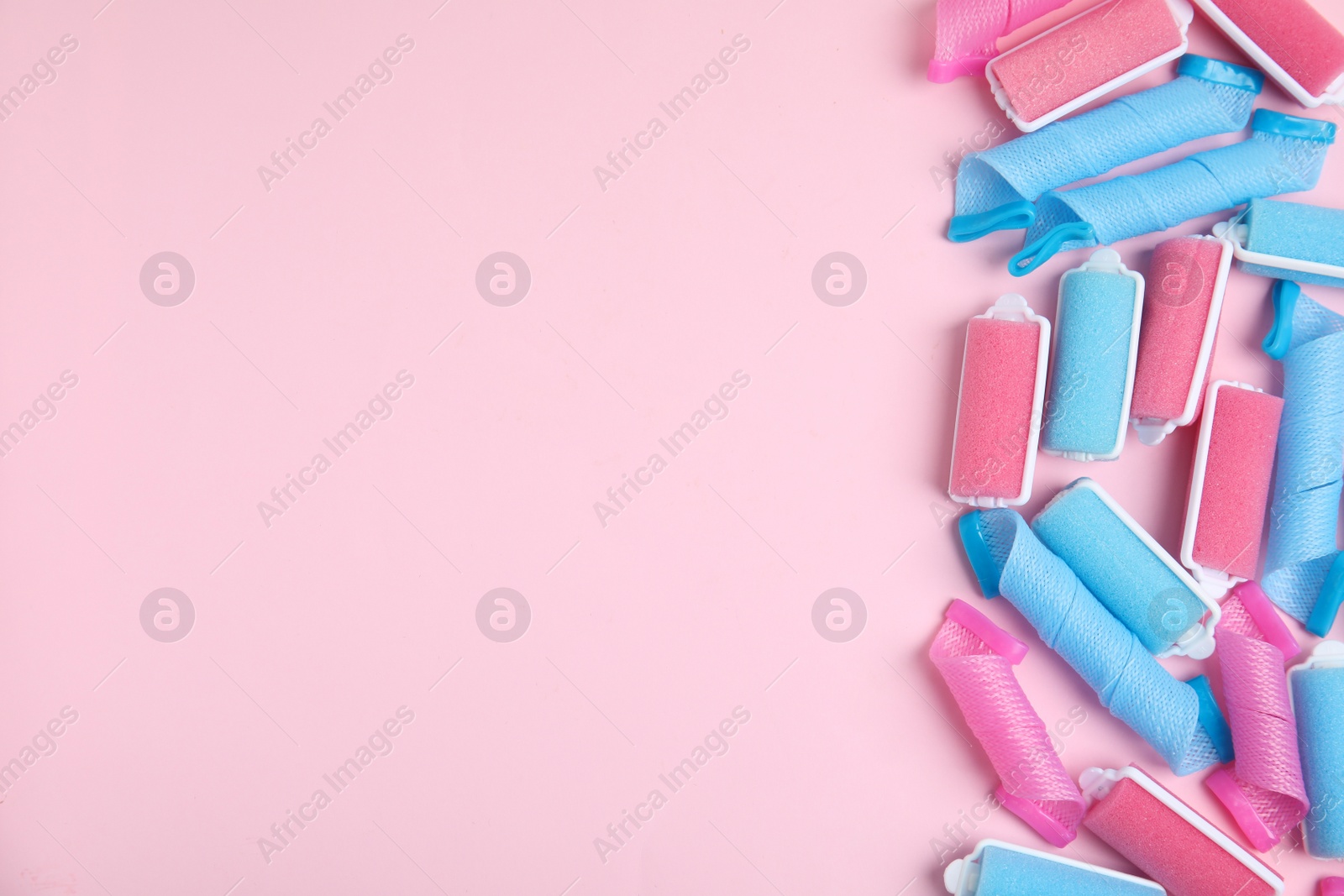 Photo of Different hair curlers on pink background, flat lay. Space for text