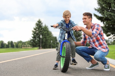 Photo of Dad teaching son to ride bicycle outdoors