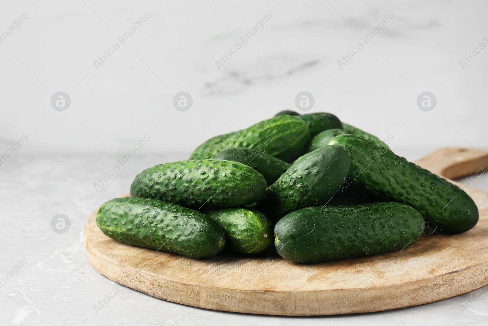 Photo of Board with fresh ripe cucumbers on white marble table