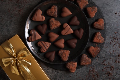 Delicious heart shaped chocolate candies and gift box on grey table, flat lay