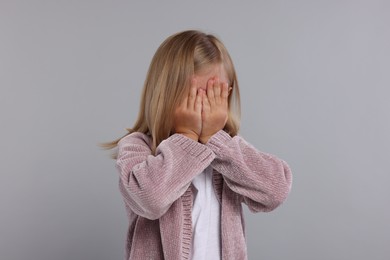 Resentful girl covering face with hands on grey background