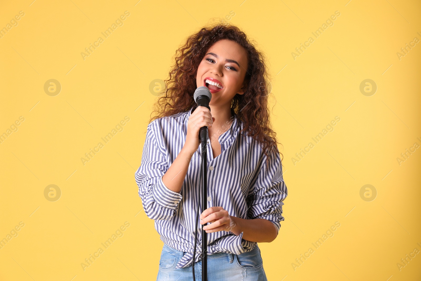 Photo of Portrait of curly African-American woman singing in microphone on color background