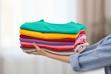 Photo of Woman holding folded clean clothes indoors, closeup. Laundry day