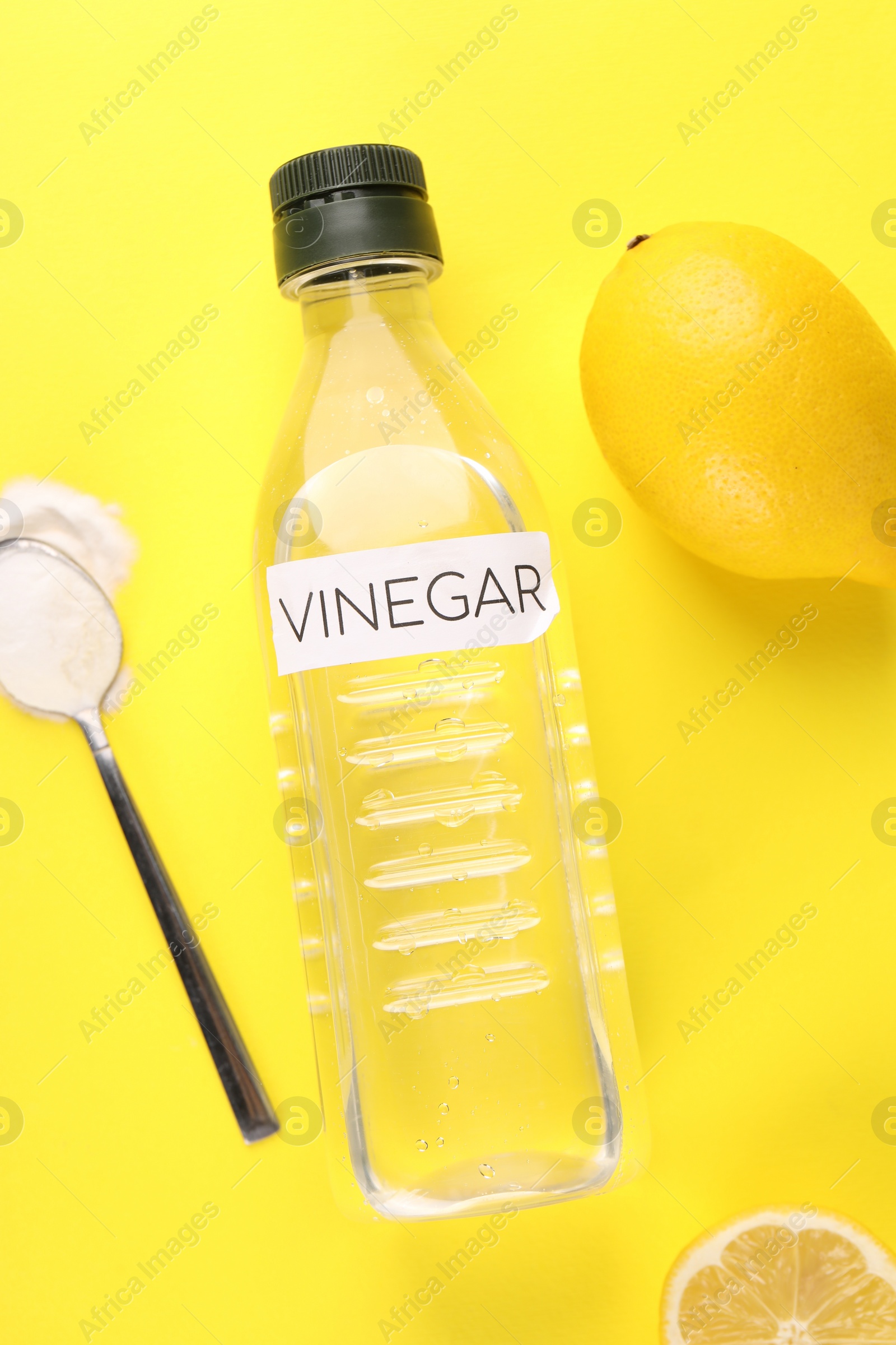 Photo of Eco friendly natural cleaners. Vinegar in bottle, lemons and spoon of soda on yellow background, flat lay