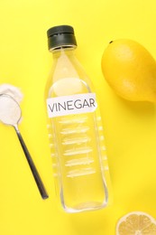 Photo of Eco friendly natural cleaners. Vinegar in bottle, lemons and spoon of soda on yellow background, flat lay