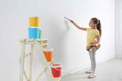 Little child painting on blank white wall indoors