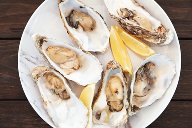 Photo of Fresh oysters with cut juicy lemon on plate, top view