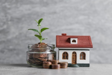 Photo of House model, jar with coins and plant on table against grey background. Space for text