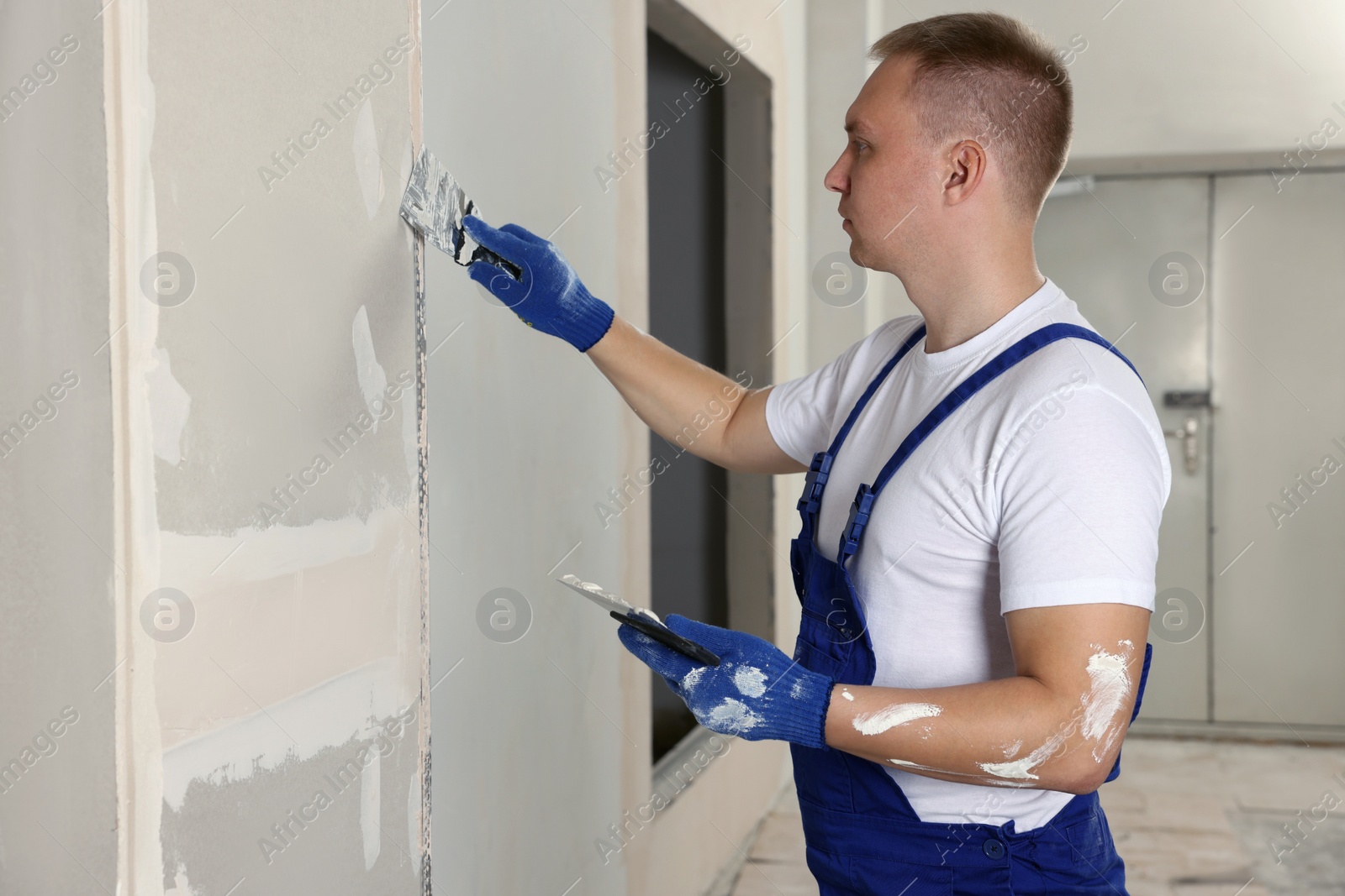 Photo of Man plastering wall with putty knife indoors. Home renovation