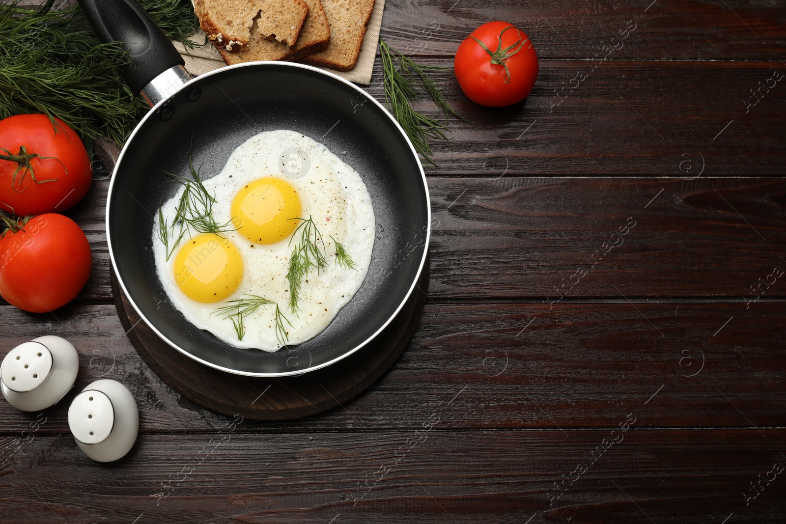 Photo of Frying pan with tasty cooked eggs, dill and other products on wooden table, flat lay. Space for text