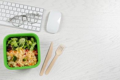 Photo of Container of tasty food, cutlery, keyboard, mouse and glasses on white wooden table, flat lay with space for text. Business lunch